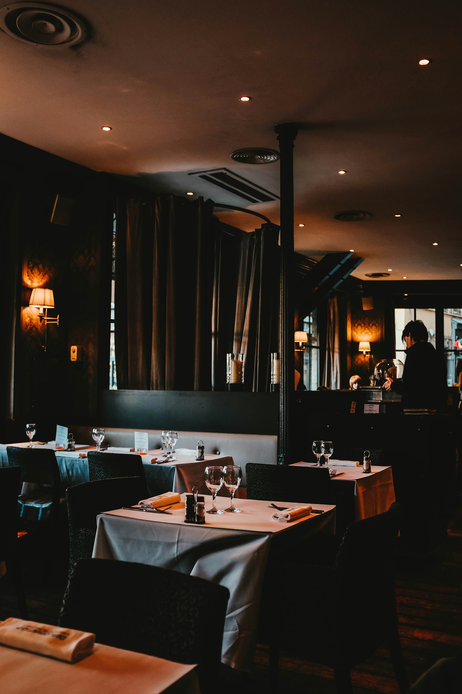 Sala della brasserie con tende di velluto, lampade da parete e tavoli apparecchiati