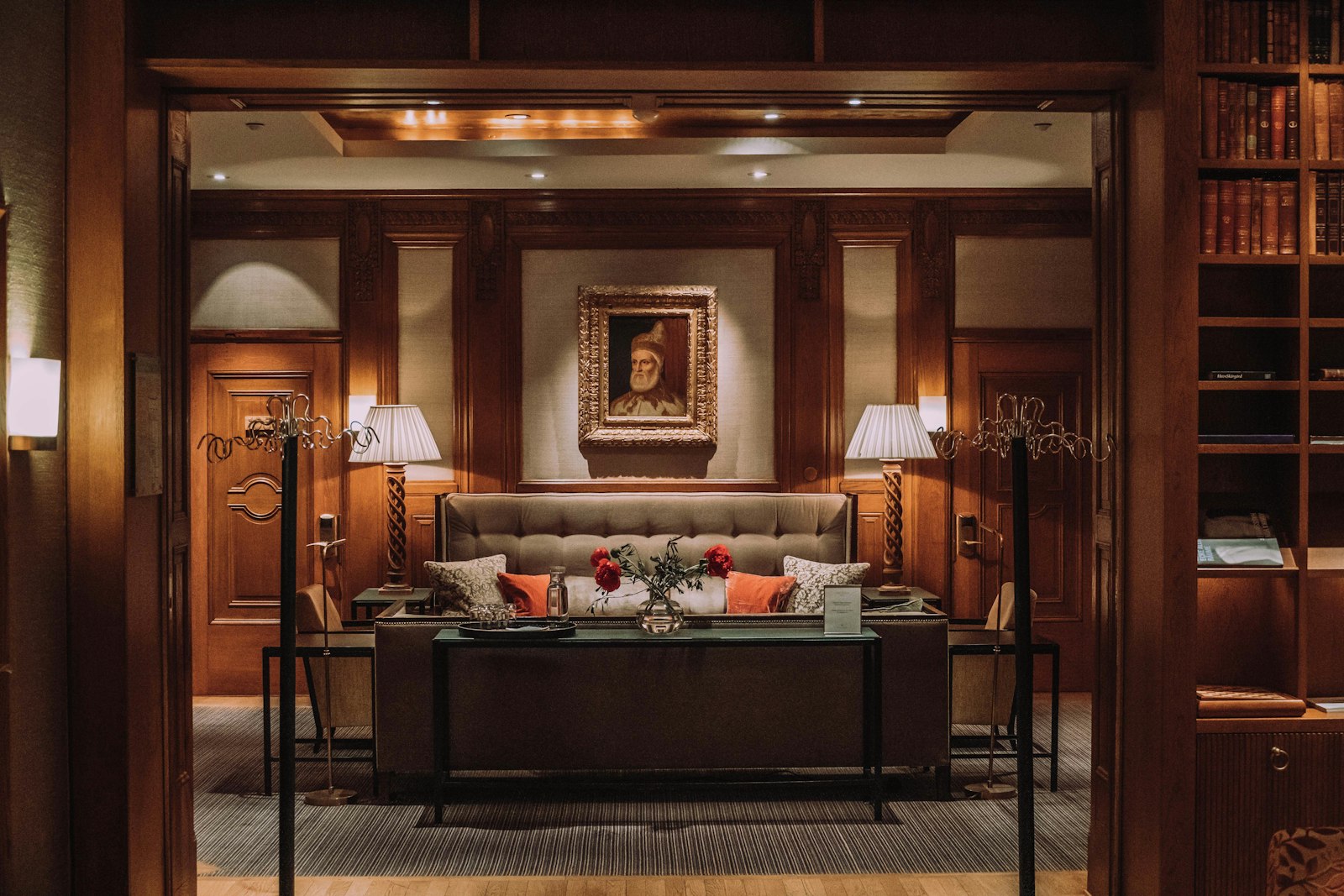 Il salotto-biblioteca dell'hotel: boiserie in noce, divano capitonné e un ritratto a olio illuminato da abat-jour