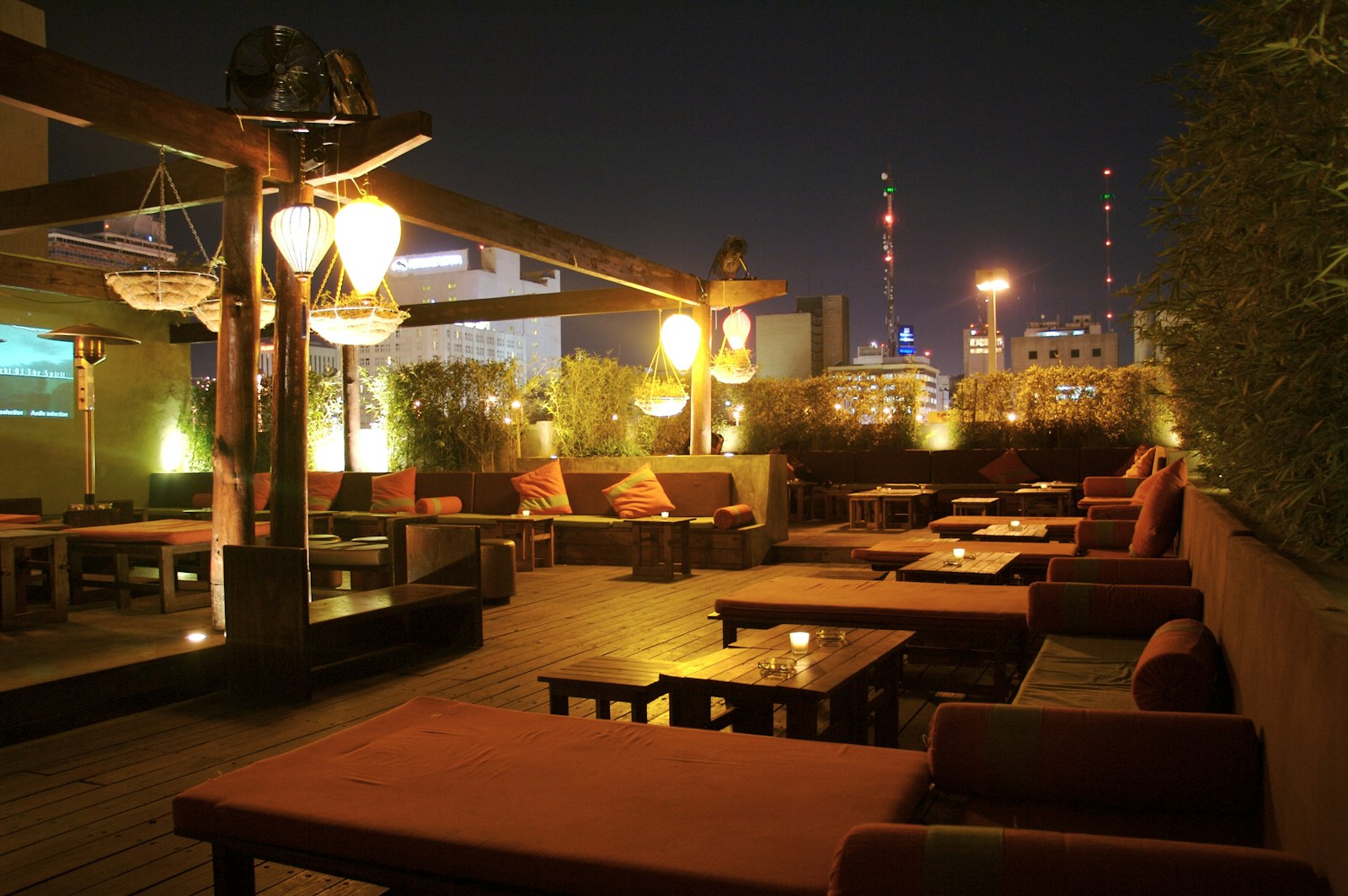 Terrazza rooftop al tramonto con lanterne calde, divani bassi e lo skyline della città sullo sfondo